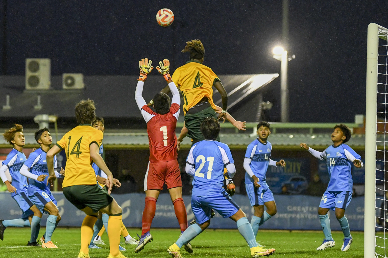 An Australian player leaps high to header the ball away from a goalie while Northern Mariana Islands players gather around.