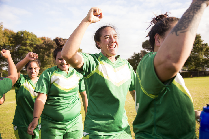A team of women in green team uniforms celebrate while on the field