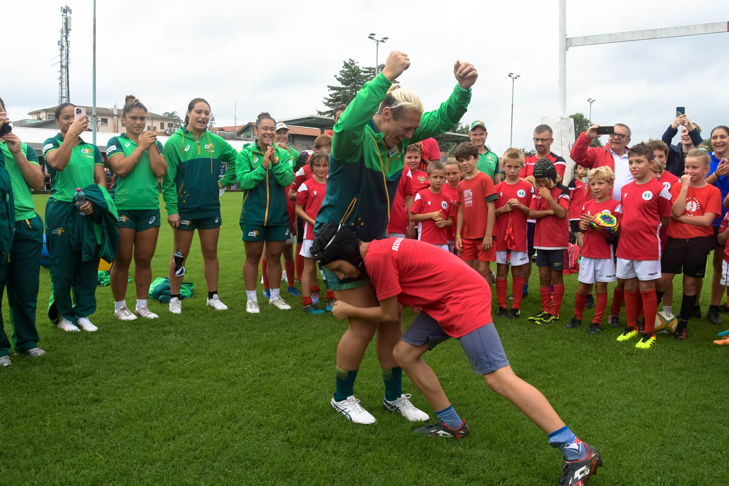 A child playfully tackles an adult rugby 7s player in front of a crowd.