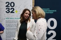 Two women standing in front of a banner featuring the 2032+ Win Well Pledge